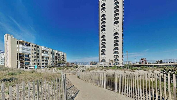 Ein Küstengebäude mit mehreren Balkonen, einem Sandweg und einem Holzzaun.
