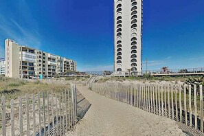A coastal building with multiple balconies, a sandy path, and a wooden fence. - Fantastic condo situated in beachfront condo with free WiFi & shared pool (Ocean City)