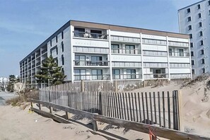 Ein mehrgeschossiges Gebäude mit Balkonen, ein Sandstrand im Vordergrund und ein Holzzaun.