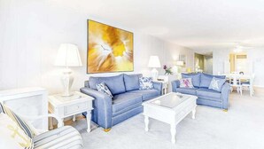 Ein modernes Wohnzimmer mit einem blauen Sofa, einem weißen Couchtisch und einem großen abstrakten Gemälde an der Wand.