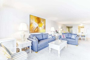 Ein modernes Wohnzimmer mit einem blauen Sofa, einem weißen Couchtisch und einem großen abstrakten Gemälde an der Wand.