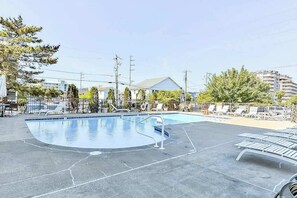 Ein Swimmingpool mit Liegestühlen, einem eingezäunten Bereich und Gebäuden im Hintergrund.