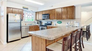 Eine Küche mit Holzschränken, einer Granit Arbeitsplatte, einem Edelstahlkühlschrank, einer Mikrowelle und einem Herd.