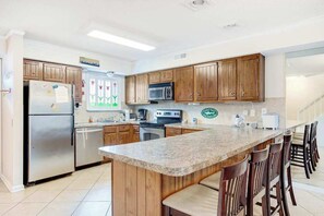 Eine Küche mit Holzschränken, einer Granit Arbeitsplatte, einem Edelstahlkühlschrank, einer Mikrowelle und einem Herd.