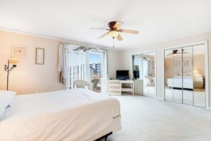 Ein Hotelzimmer mit Bett, Schreibtisch, Fernseher, Deckenventilator und Schiebetürenschrank.