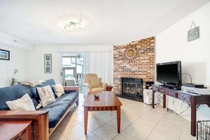 Ein Wohnzimmer mit einer Couch, einem Couchtisch, einem Fernseher, einem Kamin und einer Ziegelwand.
