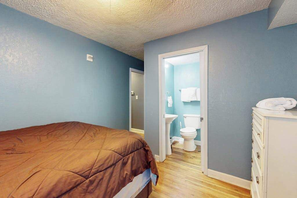 Een slaapkamer met een bed, een dressoir en een badkamer met toilet en wastafel.