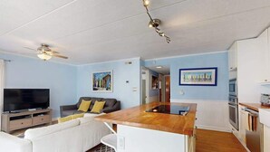 A modern kitchen with a central island, a dining area with a sofa, and a television in a living room. - Completely remodeled condo with private balcony - 100 yards to beach (Ocean City)