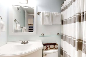 Ein Badezimmer mit Waschbecken, Spiegel, Handtuchhalter, Toilette und Duschvorhang.