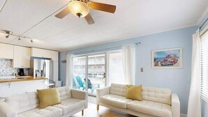 A living room with two white sofas, a ceiling fan, a kitchen area, and a balcony with a view. - Completely remodeled condo with private balcony - 100 yards to beach (Ocean City)