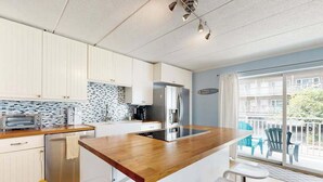 A modern kitchen with white cabinets, a wooden countertop, and a built-in stove. There is a balcony with outdoor seating visible through the glass doors. - Completely remodeled condo with private balcony - 100 yards to beach (Ocean City)