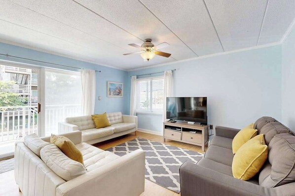 Ein Wohnzimmer mit Deckenventilator, Fernseher, zwei Sofas und einem gemusterten Teppich.