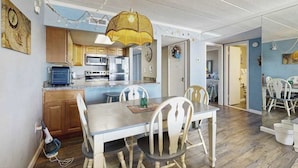 Een kleine keuken met moderne apparatuur, een eethoek met een tafel en stoelen, en een hangende lamp.