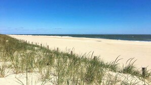 Een strand met duinen en een houten omheining.
