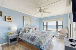 Ein Schlafzimmer mit Bett, Sessel, Nachttisch, Lampe, Deckenventilator und Fenster mit Blick.