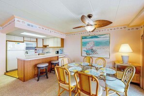 A compact hotel room with a kitchenette, a dining area with a table and chairs, a ceiling fan, and a beach-themed painting. - Bay view condo with WiFi, balcony, boardwalk, pool, tennis, & on-site dining (Ocean City)