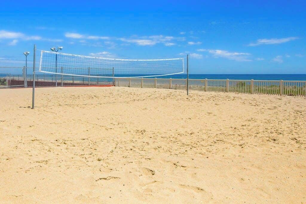 Una cancha de voleibol de playa con una red, rodeada por una cerca, y el océano al fondo.