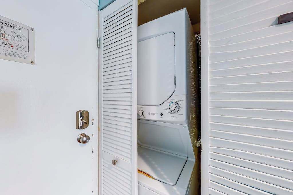 Een wasruimte met een wasmachine en droger, een deur met metalen handvat en een bord aan de muur.