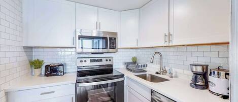 Una cocina moderna con armarios blancos, electrodomésticos de acero inoxidable y encimera blanca.