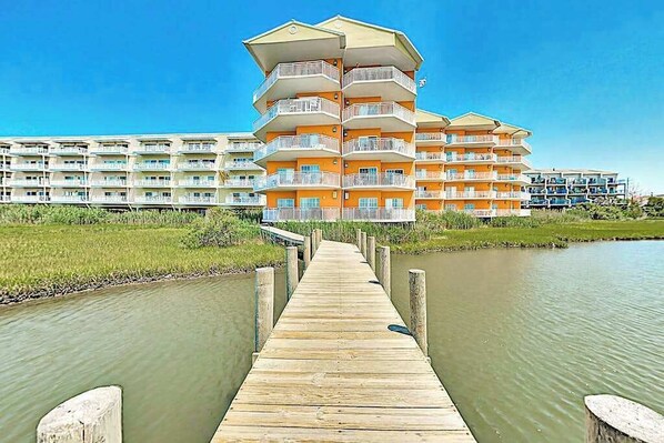 A multi-story hotel with balconies, a wooden pier leading to the building, and a body of water in the foreground. - 3rd-floor corner condo with amazing ocean views, balcony, rooftop pool, & W/D (Ocean City)