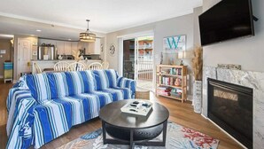 Una sala de estar con sofá, mesa de centro, chimenea, televisor y una cocina al fondo.