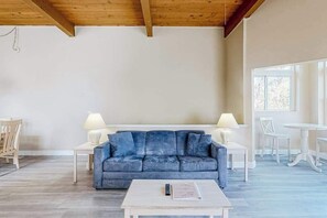 Una habitación con un sofá azul, mesas blancas y un techo de madera.