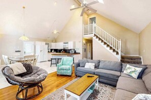 A spacious living area with a sofa, chair, and coffee table. A kitchen is visible in the background, and a staircase leads to an upper level. - A Watertown Getaway (Berlin)