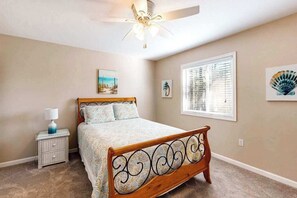 A bedroom with a bed, a nightstand, a ceiling fan, a window with blinds, and wall art.