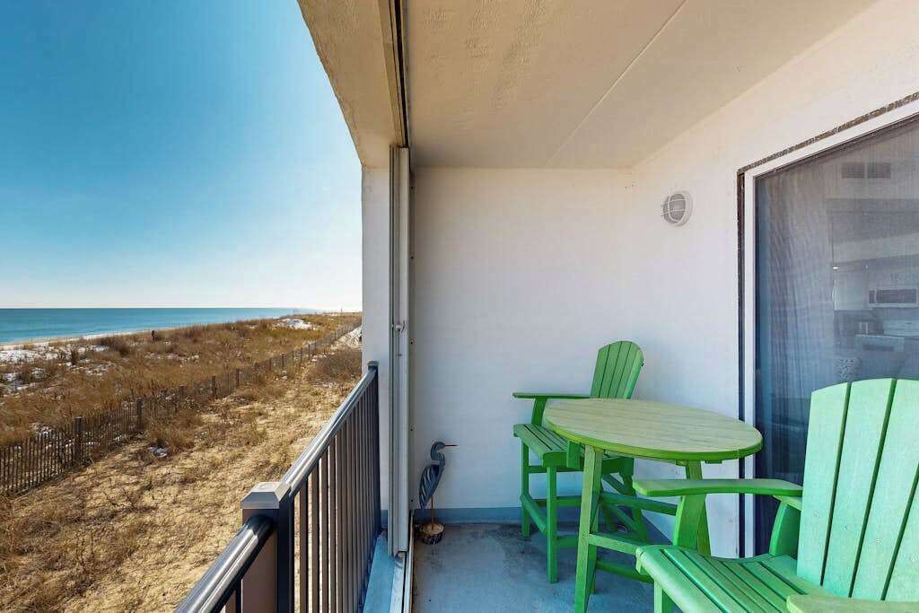 Un balcon avec vue sur la plage et l’océan, des chaises vertes et une petite table.