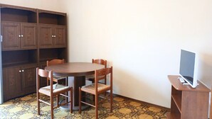 Une pièce comprenant une table ronde en bois, deux chaises, un téléviseur posé sur un meuble et des armoires encastrées en bois.