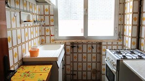 Une cuisine de taille réduite, dotée d’une fenêtre, d’un évier, d’une cuisinière et d’un petit plan de travail.