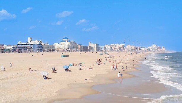 Ein Strand mit Gebäuden im Hintergrund, Menschen im Sand und dem Meer.