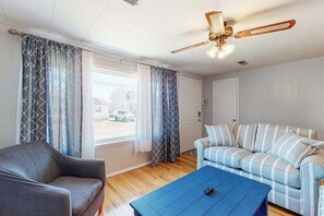 Ein Zimmer mit einer Couch, einem Sessel, einem Couchtisch, einem Deckenventilator und Blick durch ein Fenster.