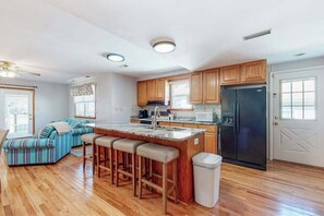 Eine Küche mit Holzschränken, einem schwarzen Kühlschrank, einer Marmorarbeitsplatte und einer Bar mit Barhocker.