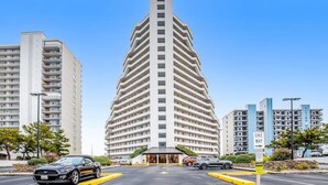 A multi-story hotel with a distinctive angular design, a parking lot with cars, and a clear sky. - Beach-View Condo at the Pyramid - Shared Oceanfront Pool, WiFi & Central AC (Ocean City)