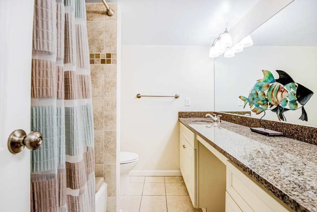 A bathroom with a shower curtain, a toilet, a sink with a mirror, and a towel rack.