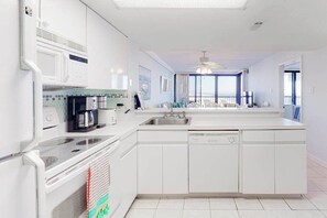 A modern kitchen with white cabinetry, a built-in oven, a coffee maker, and a view of the balcony. - Amazing ocean-view condo with AC, pools, tennis, sauna & game room (Ocean City)