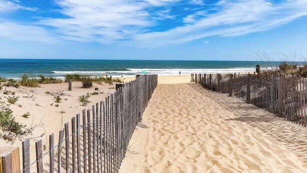 Une plage de sable bordée d’une clôture en bois, offrant une vue dégagée sur l’océan.