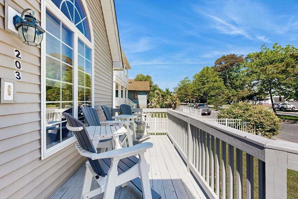 A wooden deck with outdoor seating, a white picket fence, and a clear view of the street.