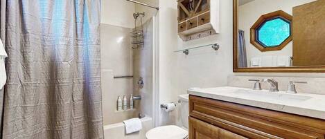 Baño con ducha, inodoro, tocador con espejo y bañera.