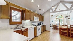 Une cuisine avec des meubles en bois, un plan de travail blanc, une cuisinière et un coin repas avec des chaises.