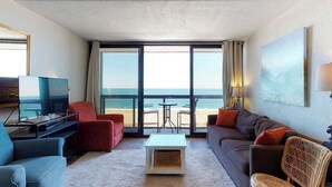 A hotel room with a balcony, a television, a sofa, a coffee table, and a view of the beach. - Delightful beachfront studio with full kitchen, balcony, pools, gym & tennis (Ocean City)