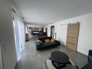 A modern living room with a sofa, a coffee table, and a dining area in the background.
