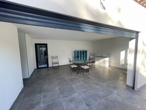 A spacious indoor area with a dining table and chairs, a kitchen area, and a door leading to another room. - Villa des amis (Caissargues)