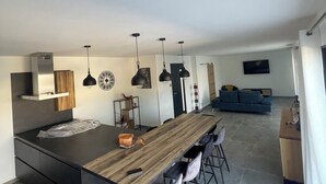 A modern kitchen with a central island, bar stools, pendant lights, and a dining area. - Villa des amis (Caissargues)