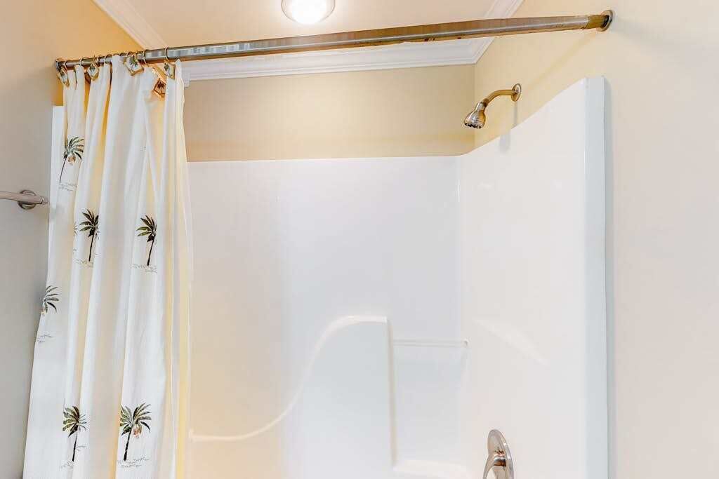 Ein Badezimmer mit Dusche, einer Duschvorhang mit Palmenmustern und einer Handstange.