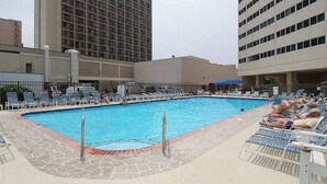 Piscina com espreguiçadeiras e um edifício alto ao fundo.