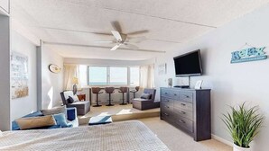 Quarto moderno com cama, televisão, ventoinha no teto e área de trabalho com cadeiras.