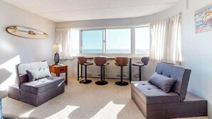 Quarto com uma cama, dois sofás, uma mesinha e um espaço bar com banquetas.