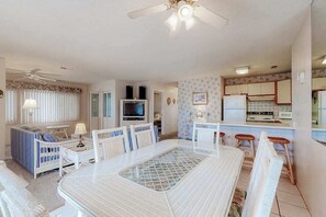 A living room with a dining table, chairs, a sofa, a TV, and a ceiling fan. - Shoreline Stepper w/ Balcony, Free WiFi, Central AC & Washer/Dryer (Ocean City)
